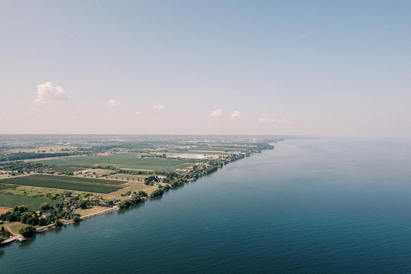 Aerial view of a coastal landscape with expansive green fields and a calm blue sea under a clear sky.