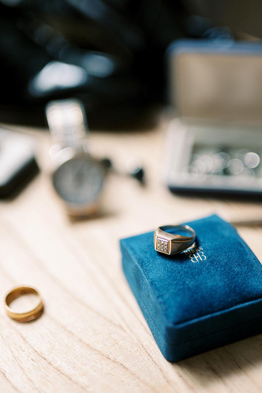 Elegant gold signet ring with diamond accents on blue jewelry box, surrounded by luxury items on a wooden surface.