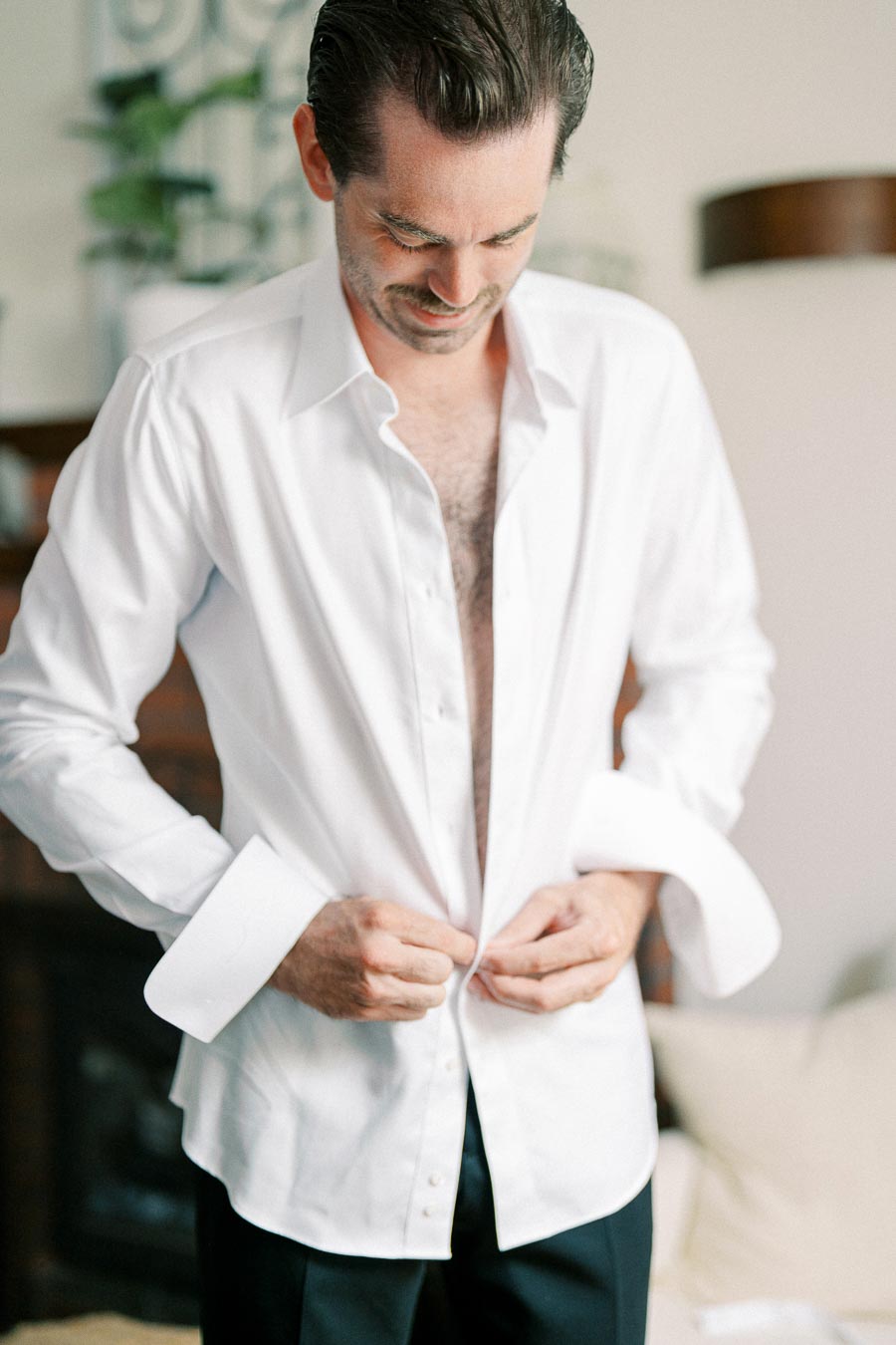 Man in white dress shirt buttoning up, preparing for a formal event.