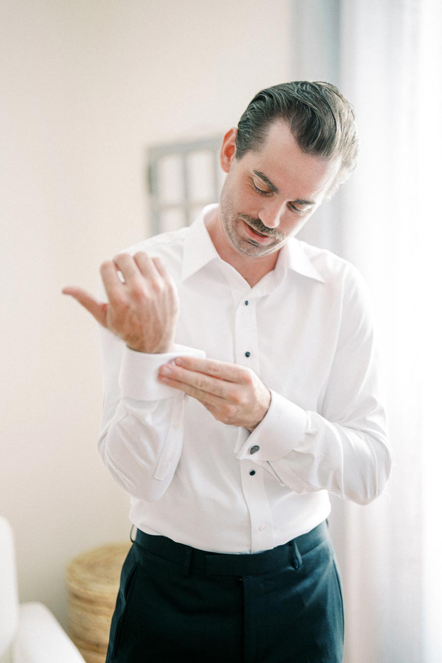 Man in a white dress shirt adjusting cufflinks, preparing for a formal event.
