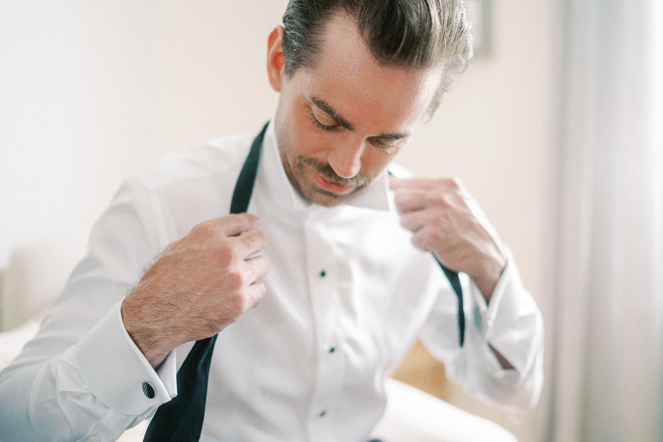 A man in a white dress shirt is adjusting his black tie, preparing for a formal event.