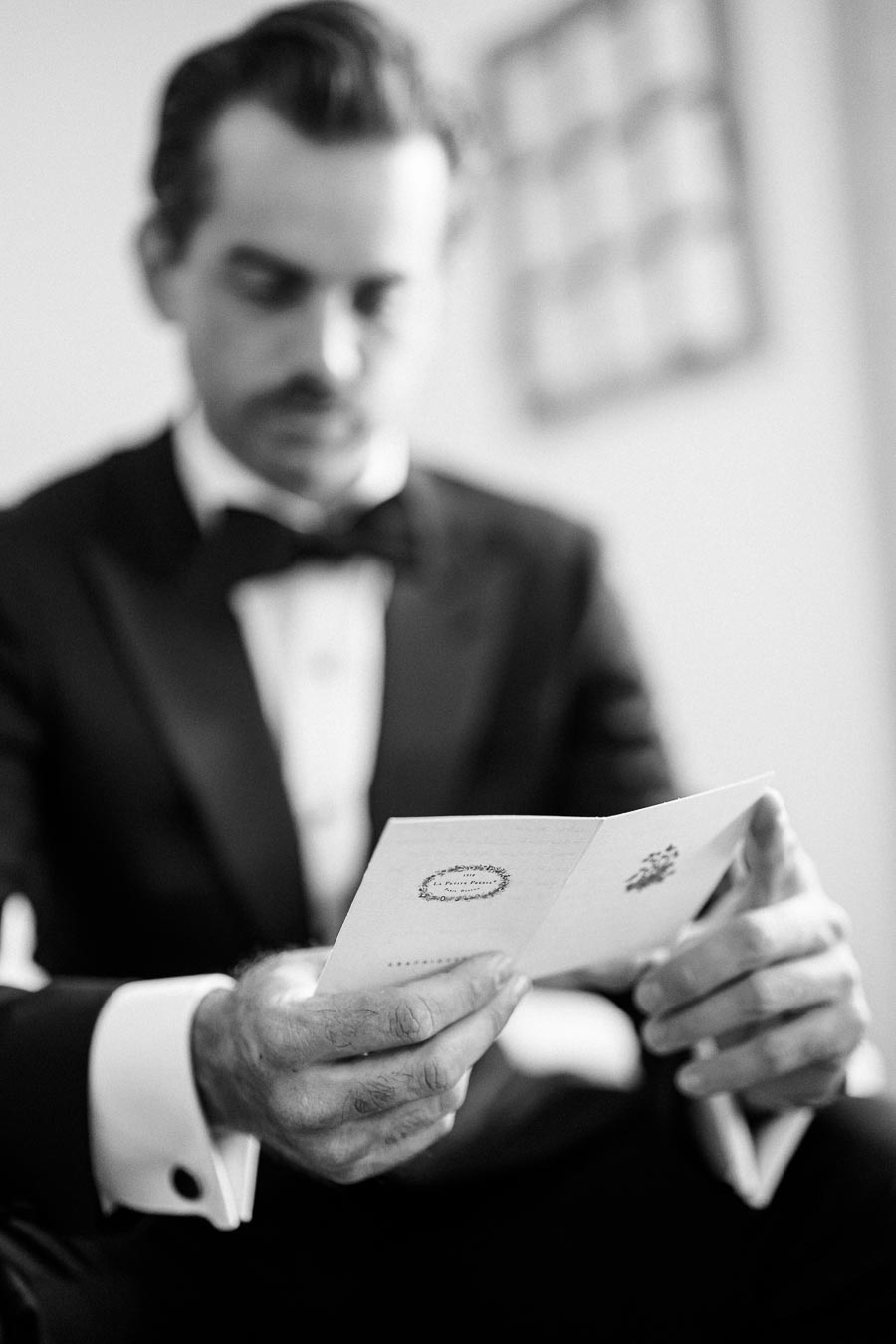 A man in a formal suit reading a letter, captured in black and white, focusing on the elegant details of his attire and the paper in his hands.