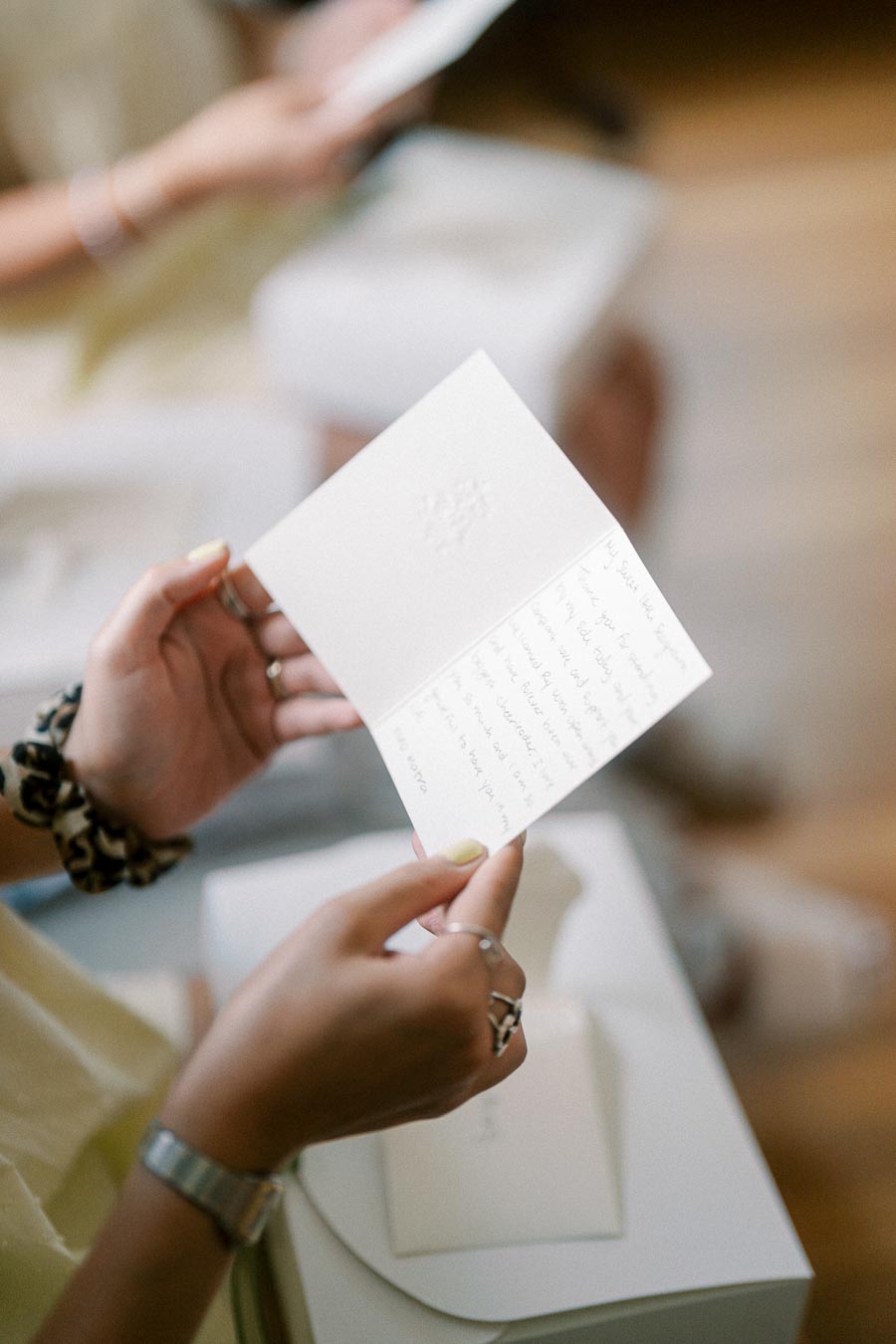 A person's hand holding an open handwritten card, displaying personal messages on elegant stationery, with a soft focus background.
