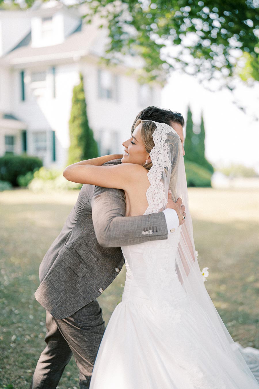 Bride and groom embracing in front of a charming white house on a sunny day, highlighting wedding joy and picturesque outdoor setting.