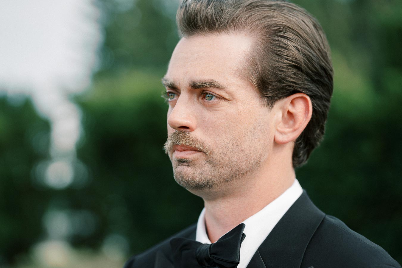 Portrait of a man in a tuxedo looking thoughtful with a blurred green background.