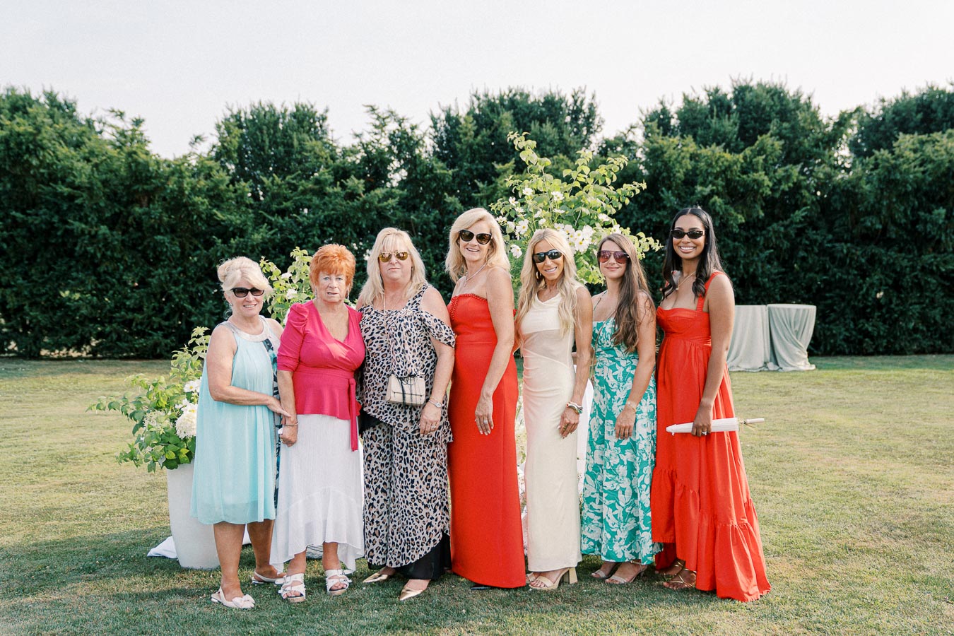 Group of women in colorful dresses posing outdoors at a garden event.
