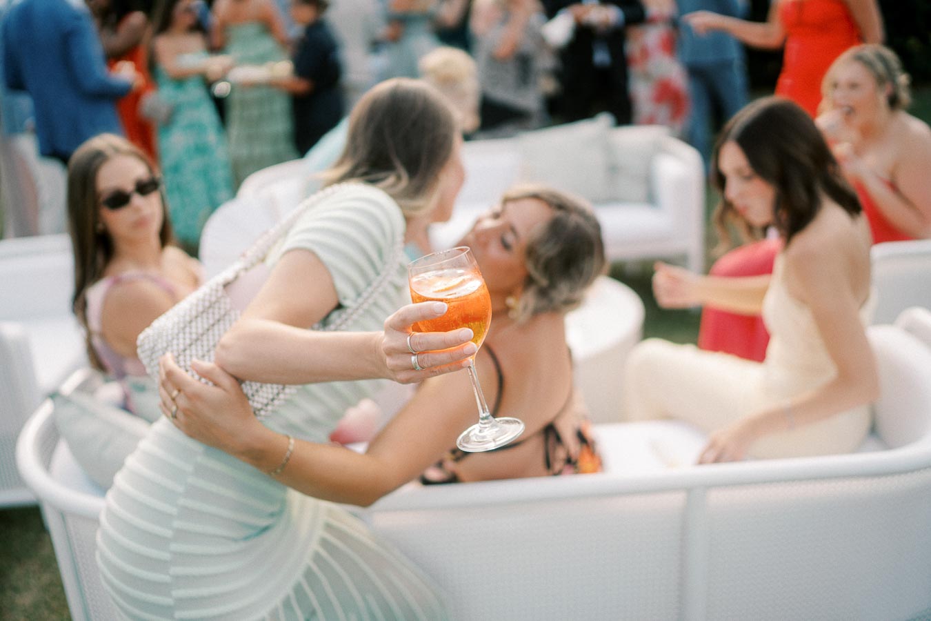 Women enjoying a social gathering with drinks, mingling on white outdoor furniture in a stylish setting.