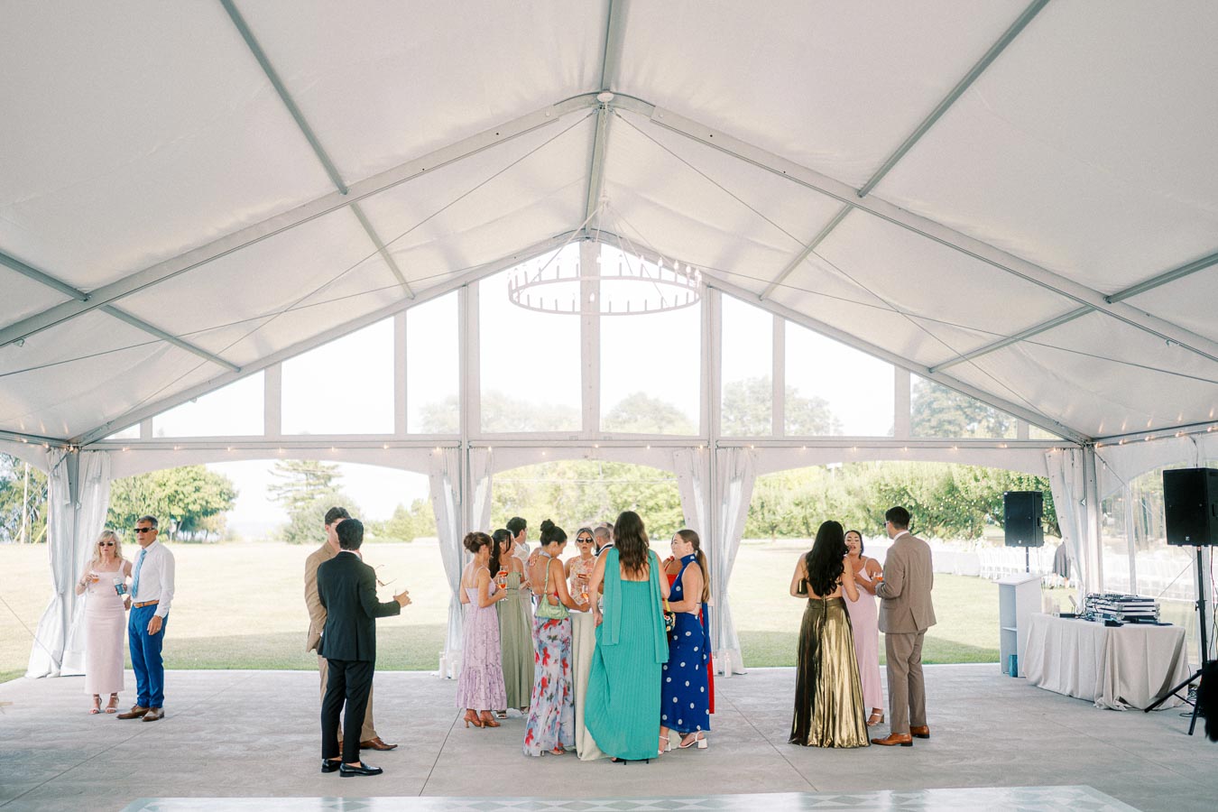 Guests mingling inside a white wedding tent, elegantly dressed, during a daytime outdoor reception.
