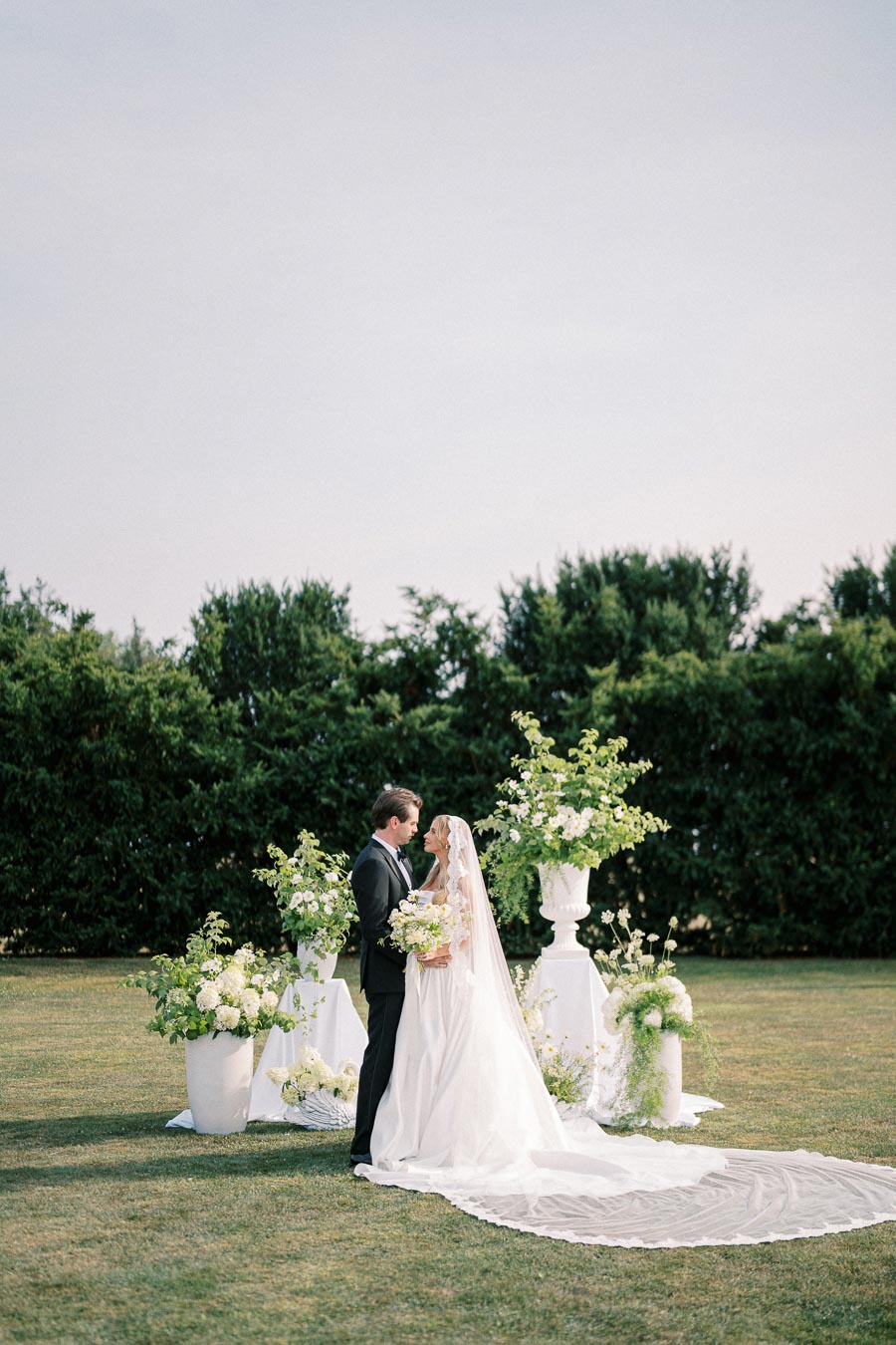 Bride and groom standing outdoors amid lush greenery and elegant floral arrangements, exchanging vows on their wedding day.