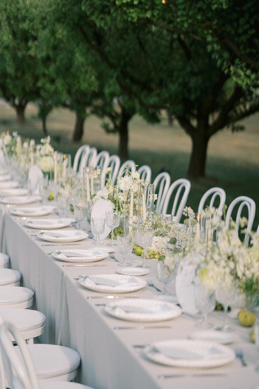 Elegant outdoor dining table setup with white chairs and floral decorations, perfect for a wedding or garden event.