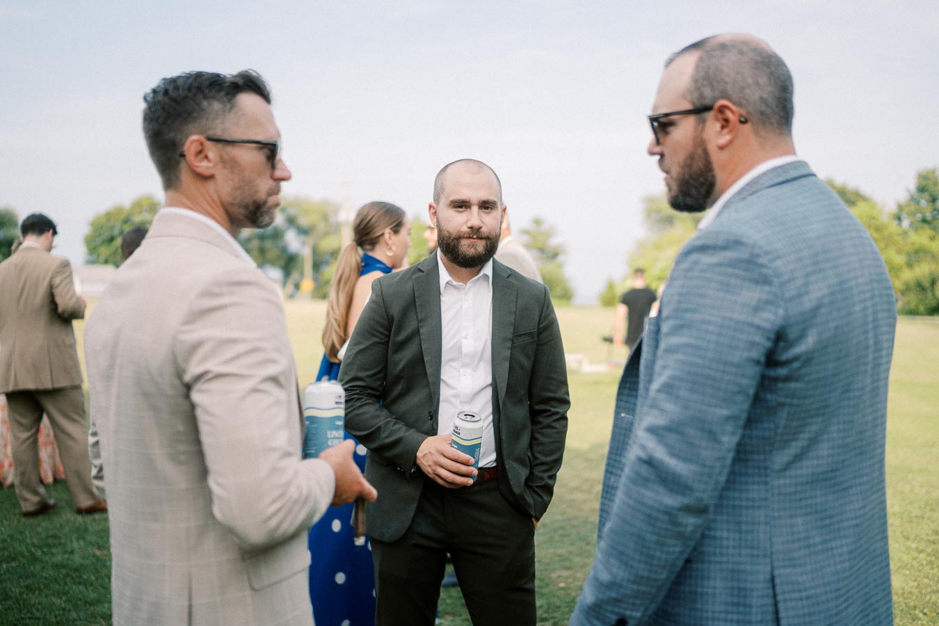 Group of men in formal attire holding drinks while socializing outdoors at an event.