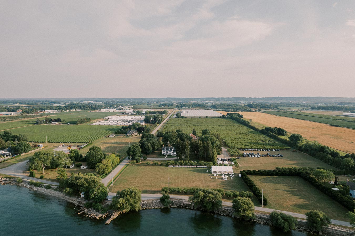 Aerial view of expansive farmland featuring agricultural fields, greenhouses, and a waterfront on a sunny day.