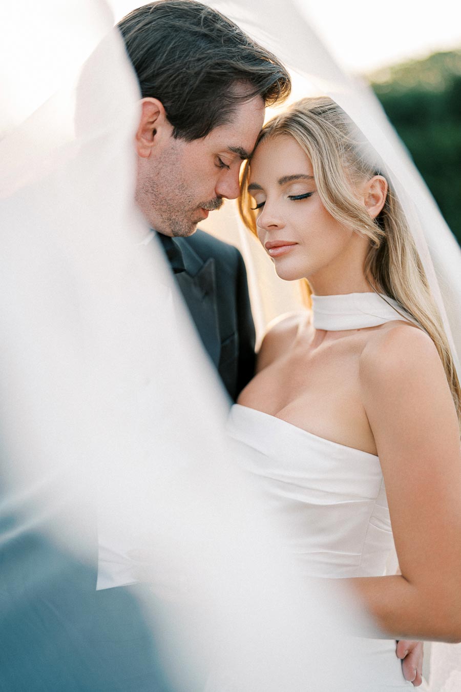 A bride and groom intimately embracing under a flowing veil, showcasing elegance and romance on their wedding day.