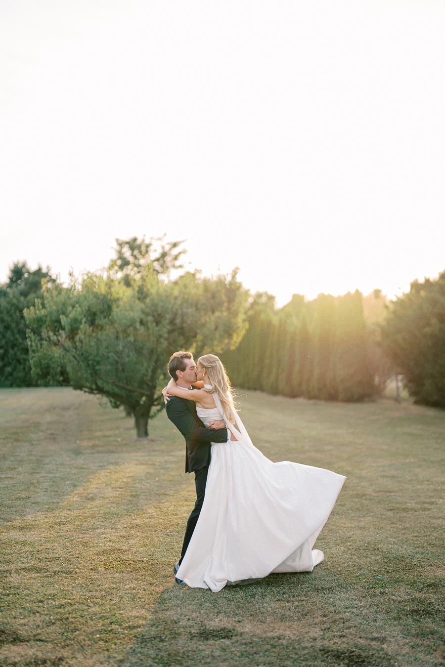 A bride and groom embrace in a romantic outdoor setting during golden hour, surrounded by lush greenery, capturing a beautiful wedding moment.