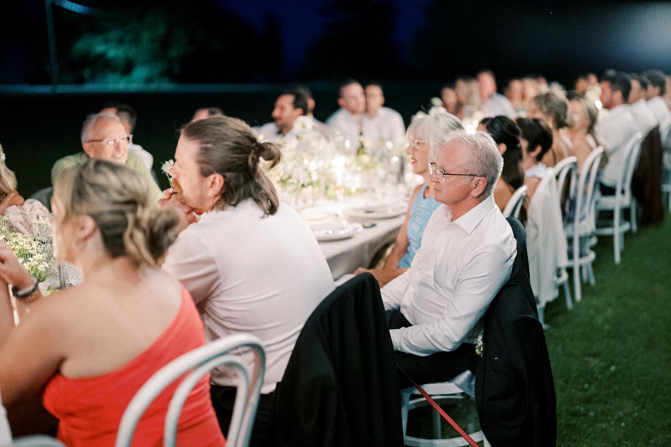 Guests seated at an elegantly decorated outdoor wedding reception table during an evening celebration, engaged and enjoying the event.