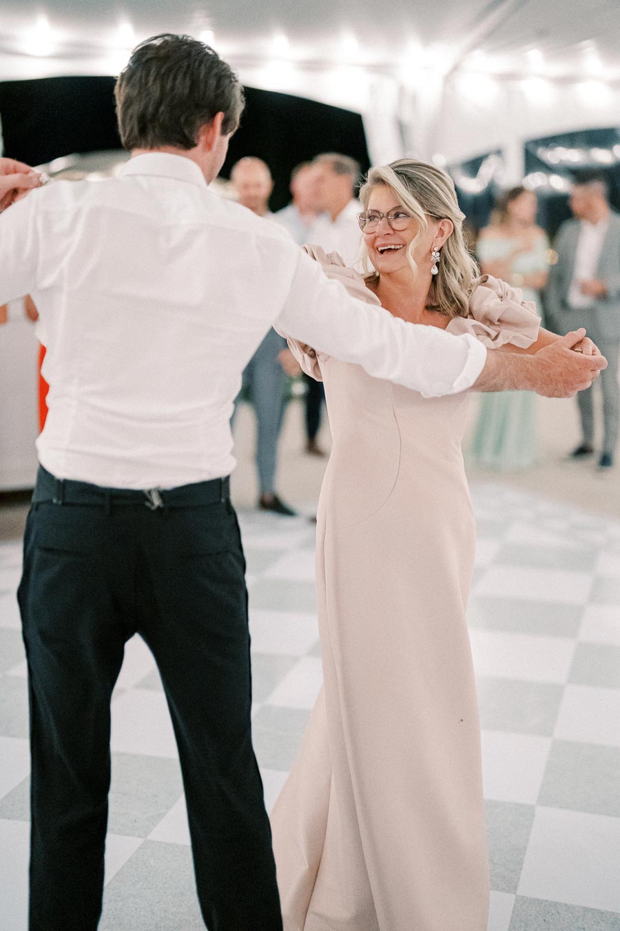 A couple dancing joyfully at an elegant event under warm lights, with guests in the background, showcasing a lively celebration atmosphere.
