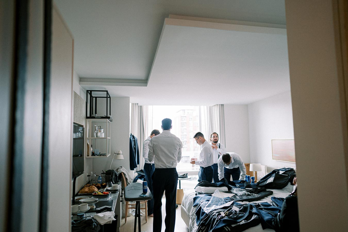 Groomsmen preparing for a wedding in a hotel room, organizing suits and accessories.
