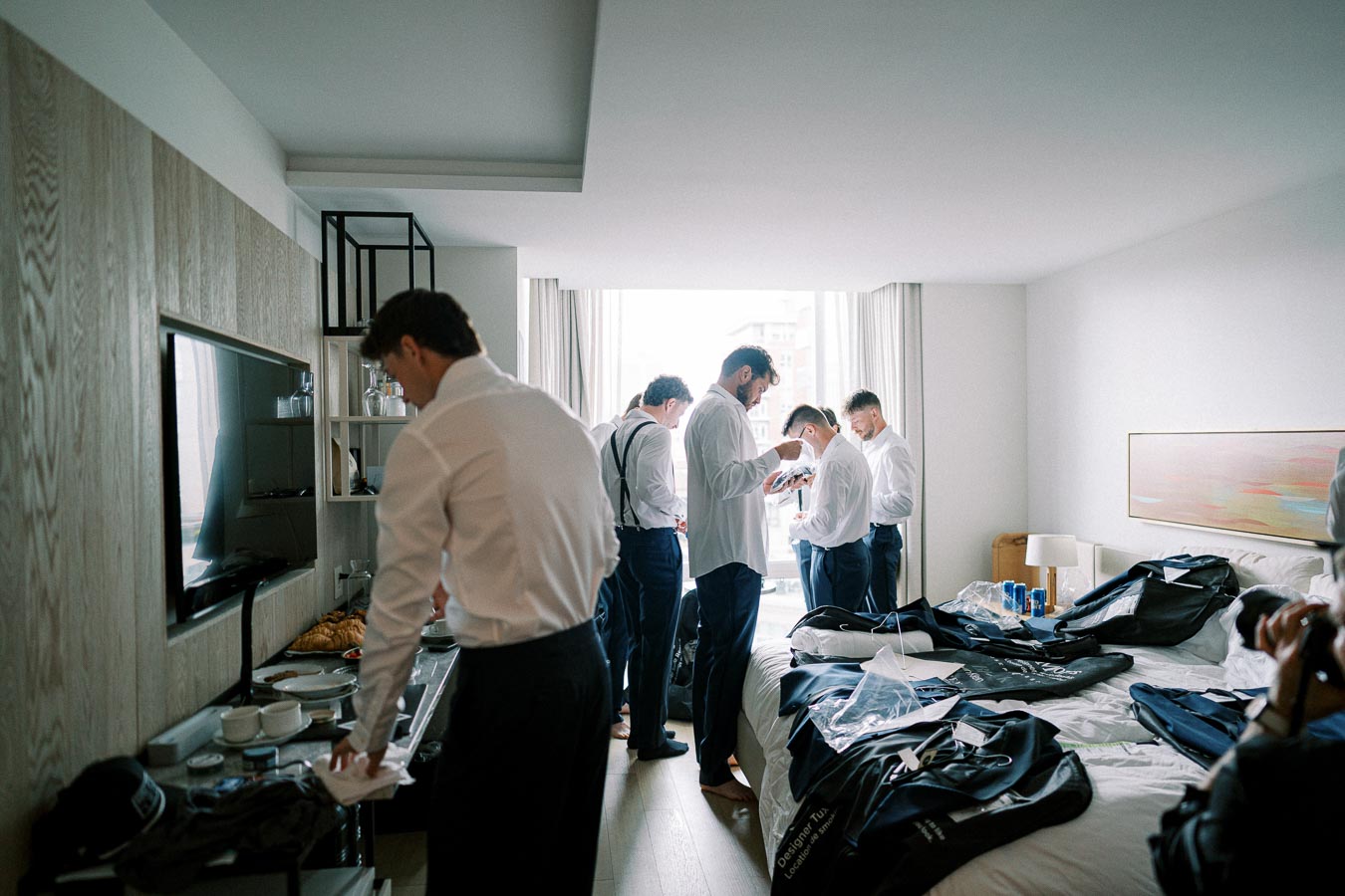 Groom and groomsmen getting ready in a modern hotel room with suits and accessories, highlighting wedding preparation moments.