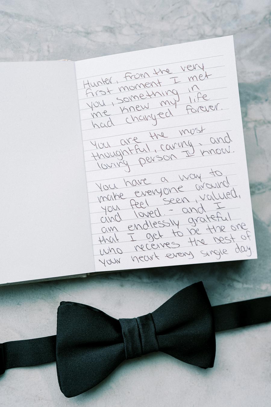 Open greeting card with handwritten heartfelt message on marble surface, accompanied by a black bow tie, conveying emotions and personal sentiments.