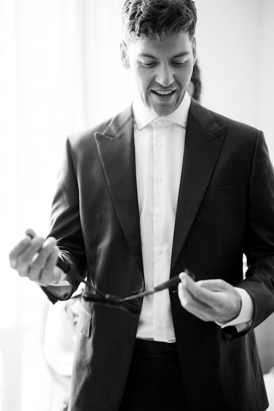 Black and white photo of a man in a suit adjusting his tie, preparing for a formal event, showing attention to detail and elegance.
