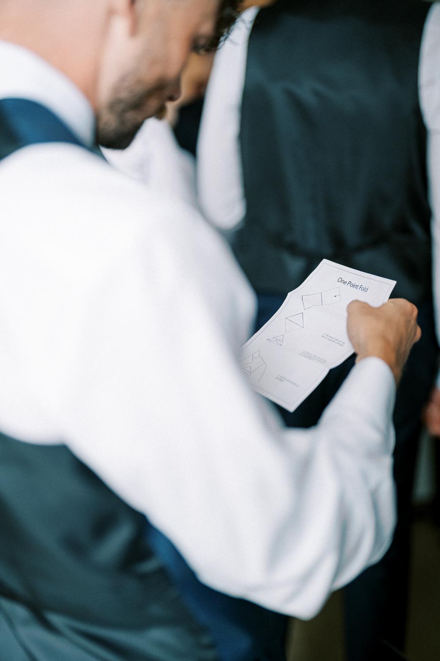 A person in formal attire holding a paper with origami instructions, focusing on precise folding steps before an event.