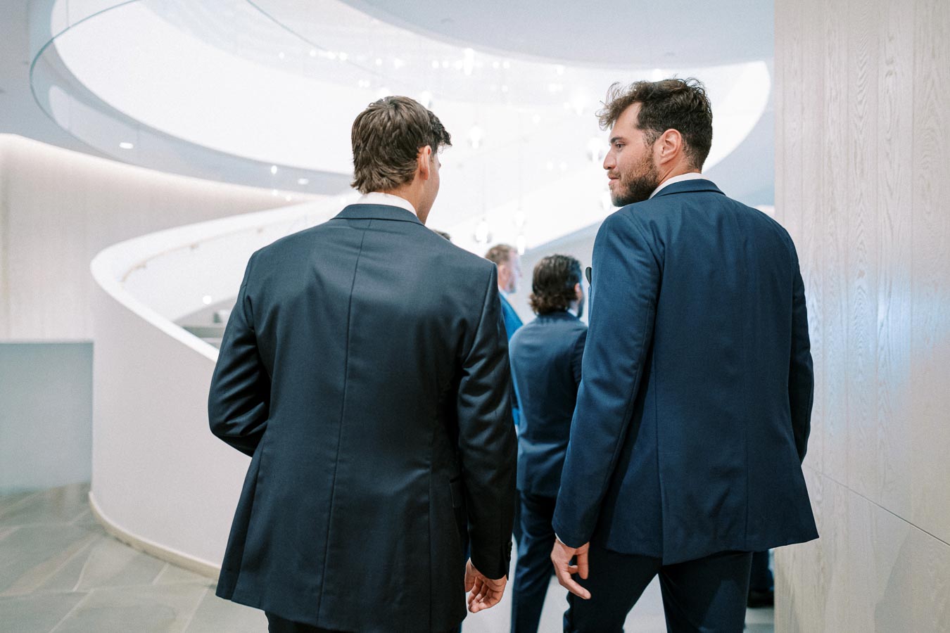 Business professionals in suits walking inside a modern office building with a spiral staircase, emphasizing a corporate and professional environment.