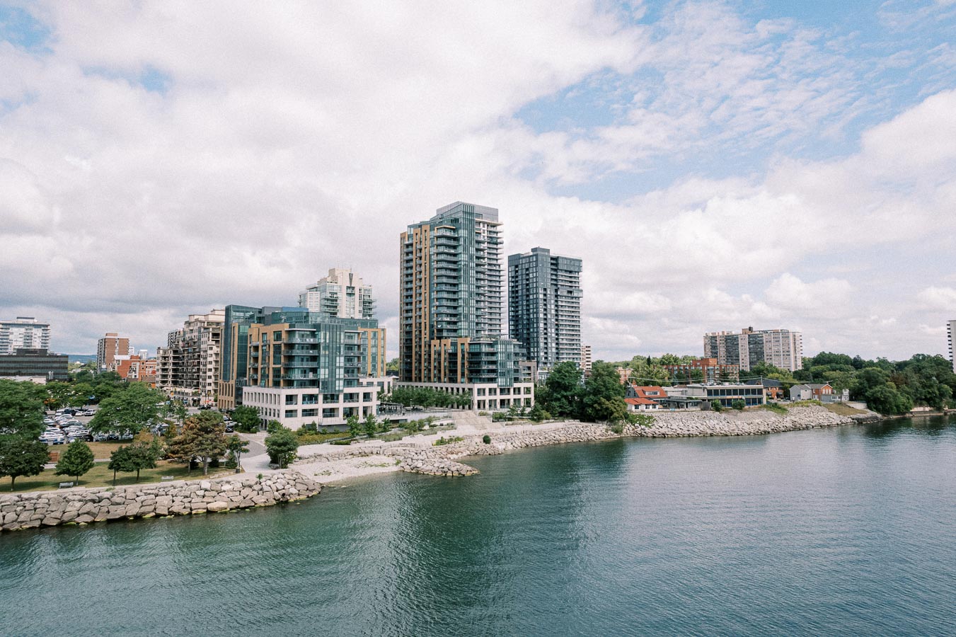 Modern high-rise buildings and waterfront view under a partly cloudy sky, featuring urban architecture and natural scenery.
