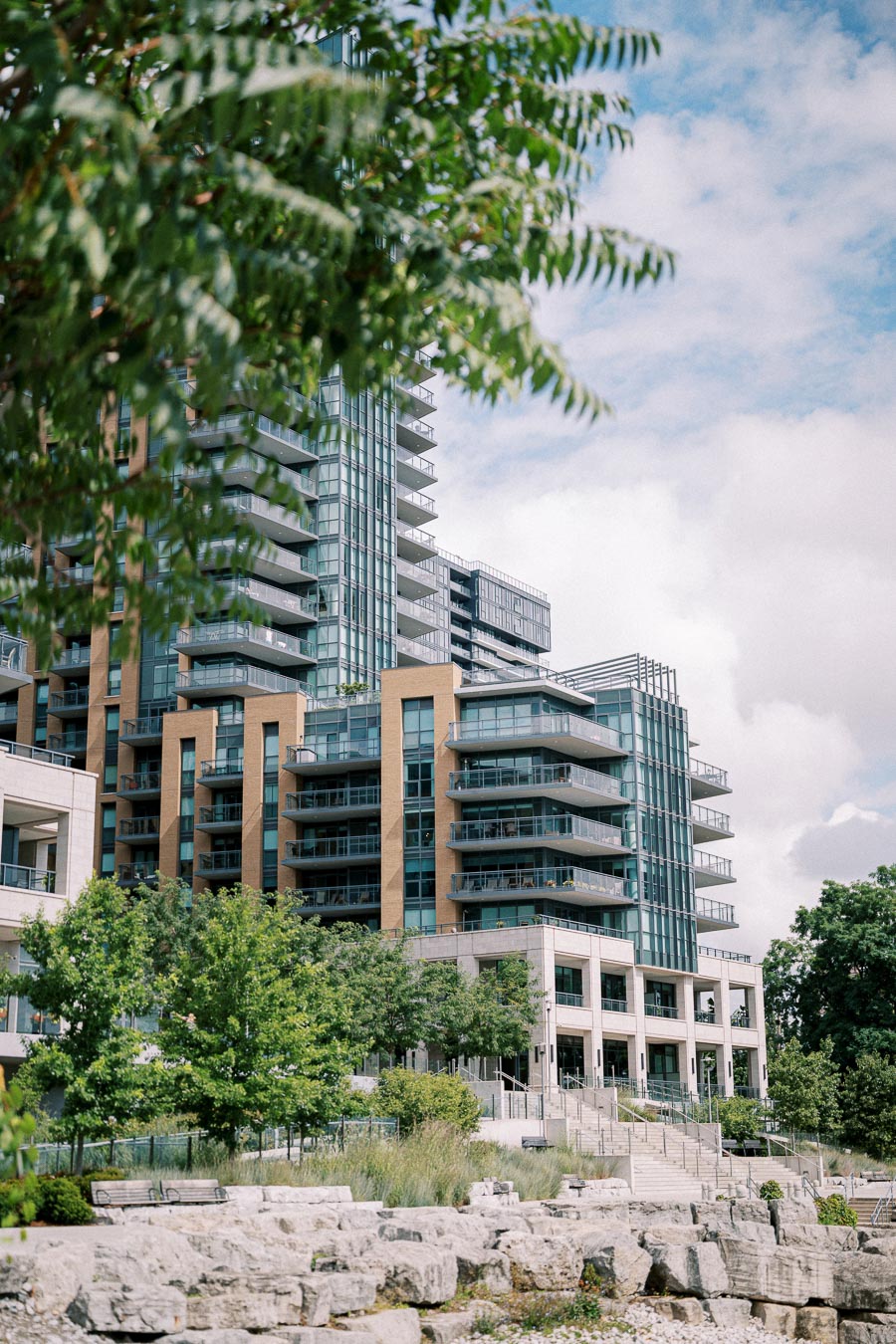 Modern residential buildings with glass balconies surrounded by lush greenery under a partly cloudy sky