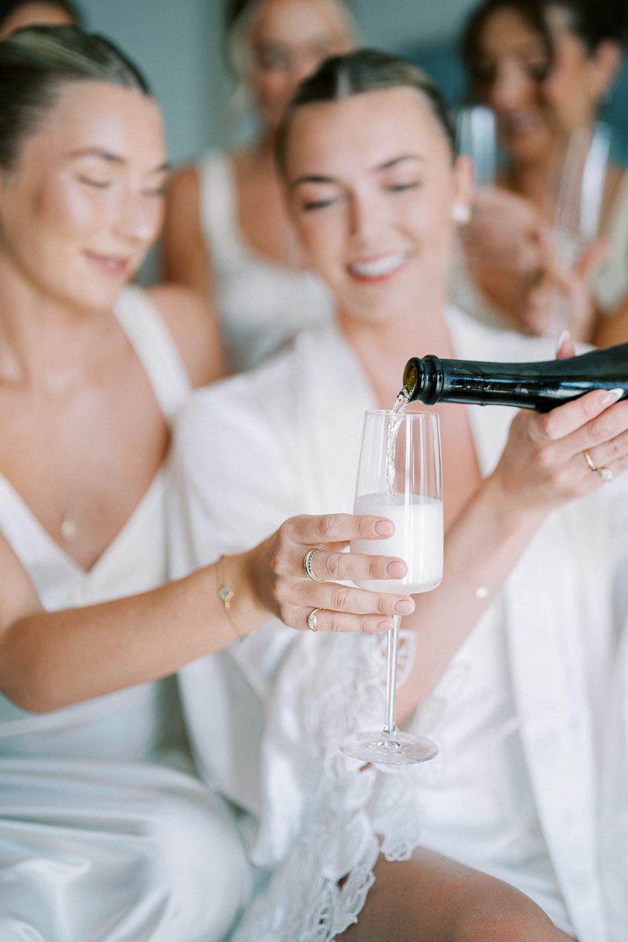 Women in elegant attire enjoy a celebratory moment as one pours champagne into a flute glass, showcasing joy and togetherness.