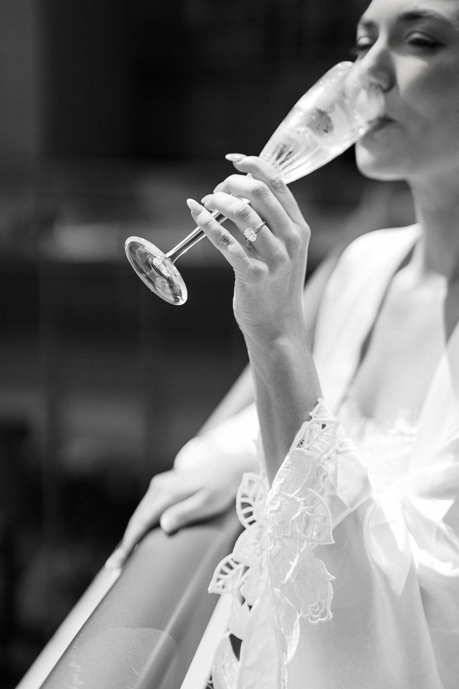 Black and white image of a woman in a lace robe, holding a champagne glass with a visible engagement ring.