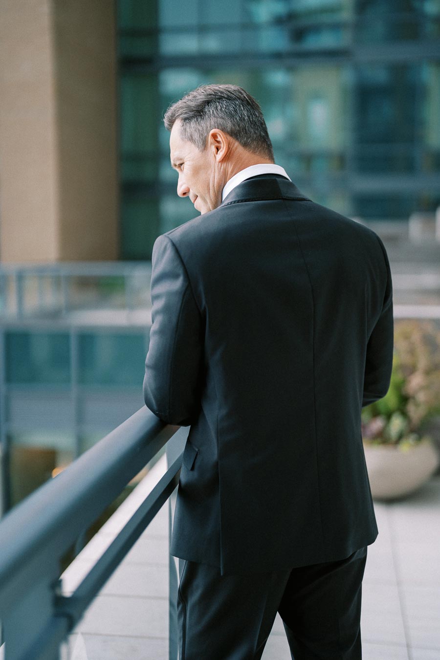 A businessman in a black suit looking over a balcony in an urban office setting, suggesting professionalism and contemplation.
