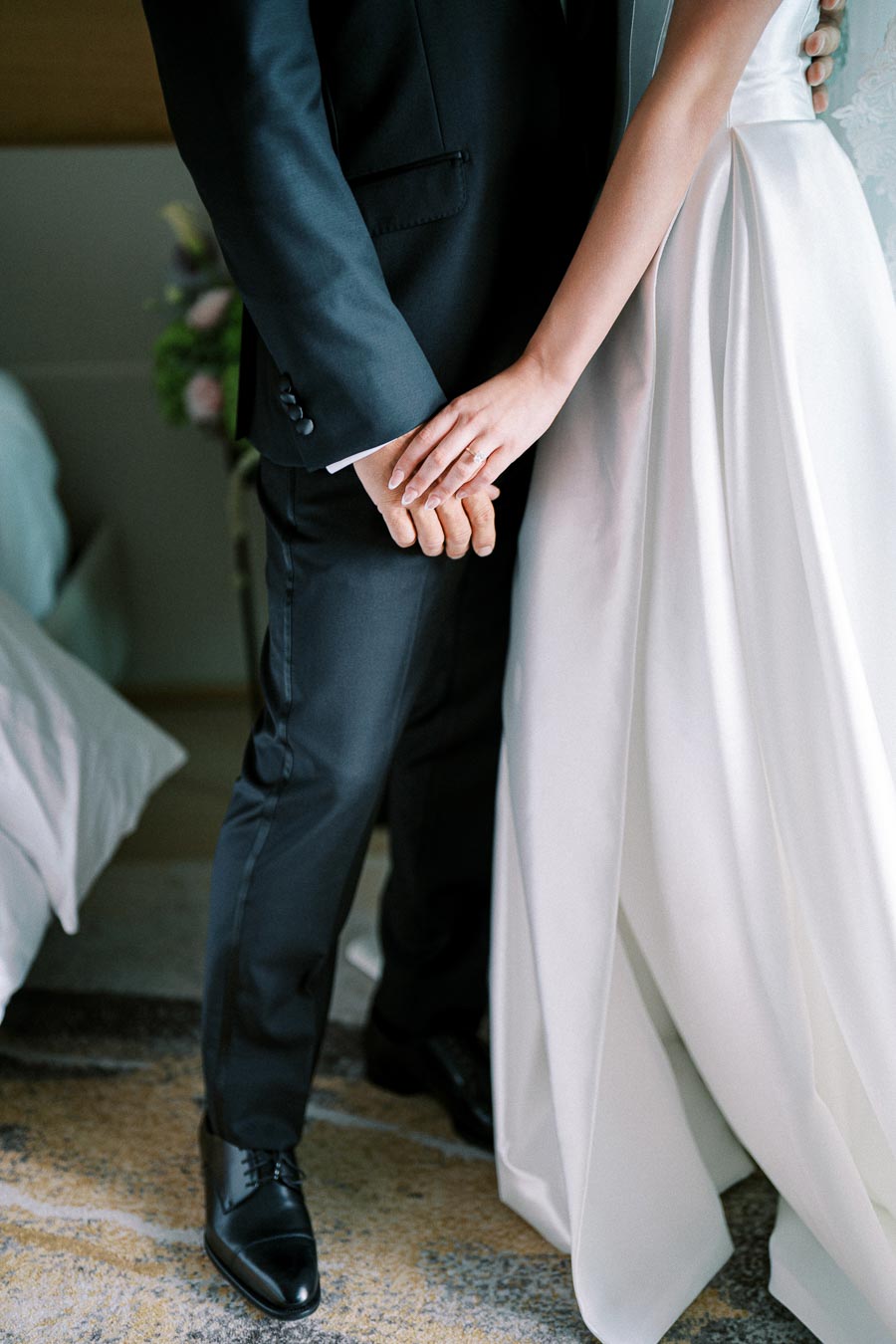 A couple on their wedding day, with the bride in a white gown and the groom in a black suit sharing an intimate moment while holding hands in soft natural lighting.