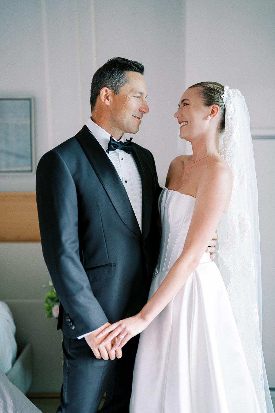 Elegant bride and groom in wedding attire holding hands and smiling at each other, capturing a romantic moment on their special day.