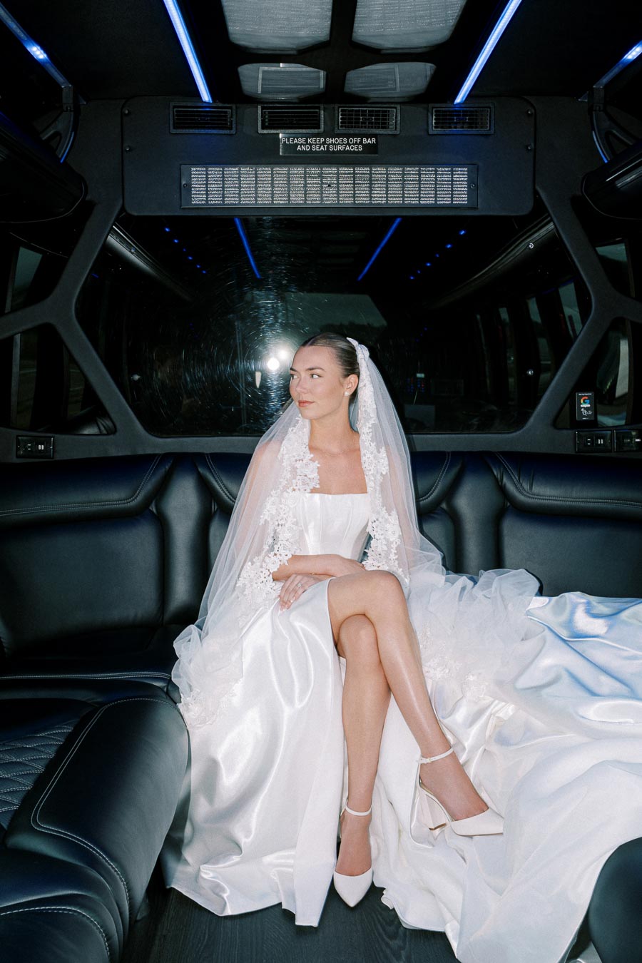 Bride in a luxurious white gown and veil sitting inside a stylish limousine, showcasing elegant bridal fashion on a wedding day.