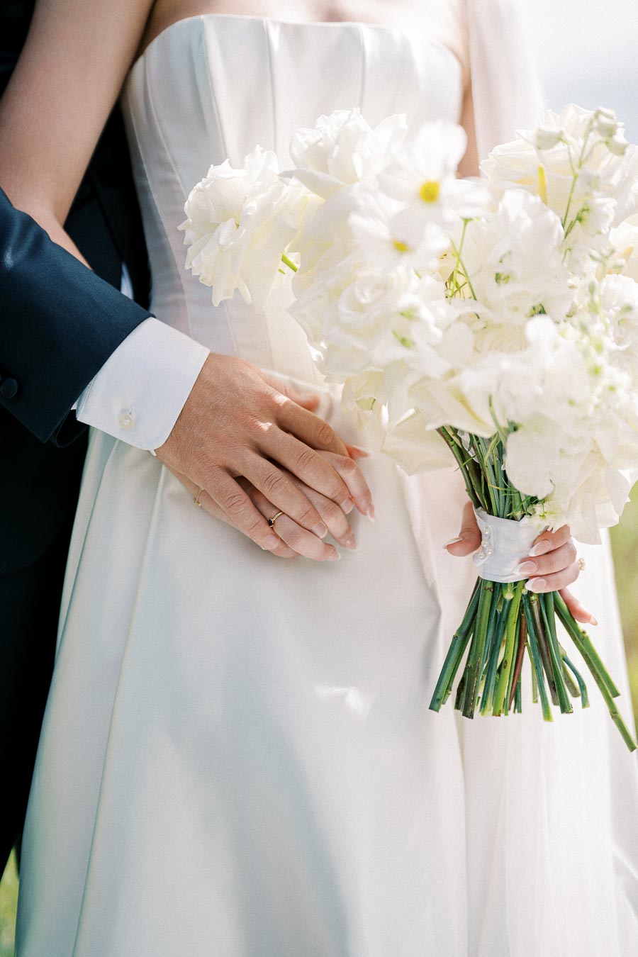Bride holding white bouquet with groom's hand resting on her waist.