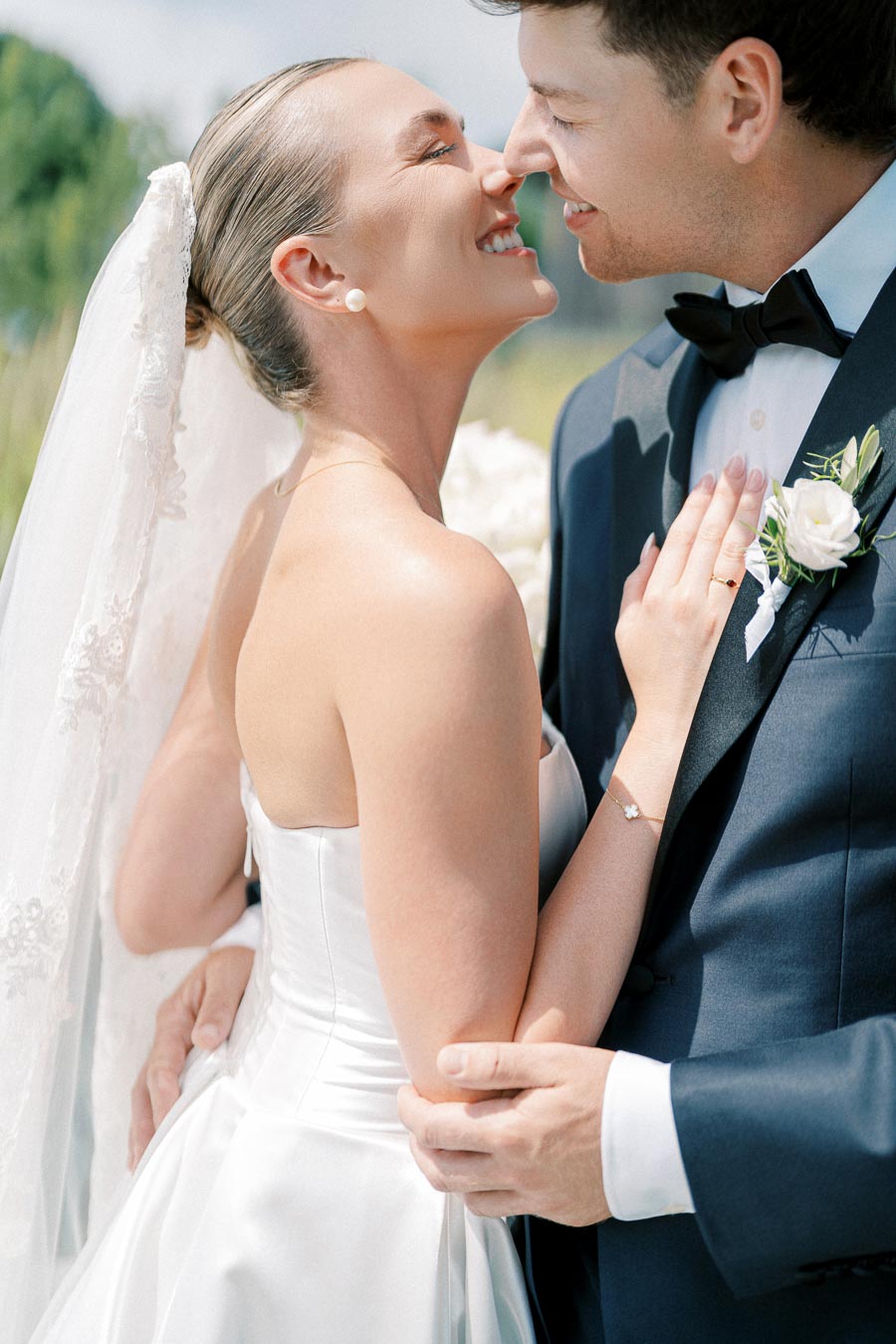 Joyful bride and groom embrace on their wedding day, bride in elegant white gown with lace veil, groom in sleek black tuxedo with floral boutonniere