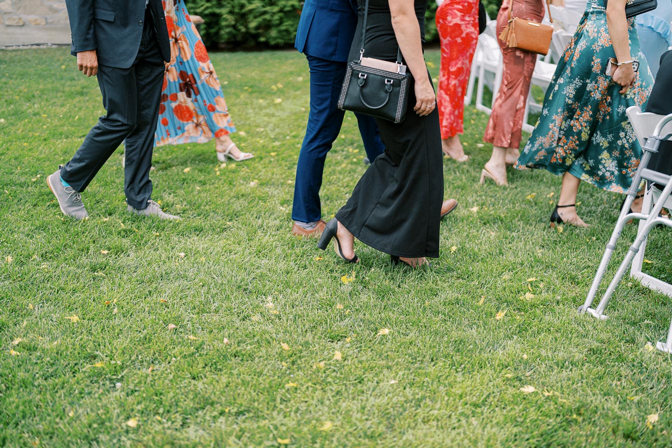 Guests in formal attire walking on green grass at an outdoor event, showcasing colorful dresses and suits.