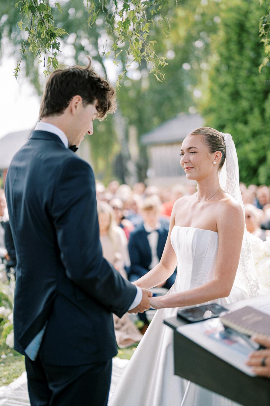 Wedded couple joyfully exchanging vows outdoors, surrounded by lush greenery, during a beautiful wedding ceremony.