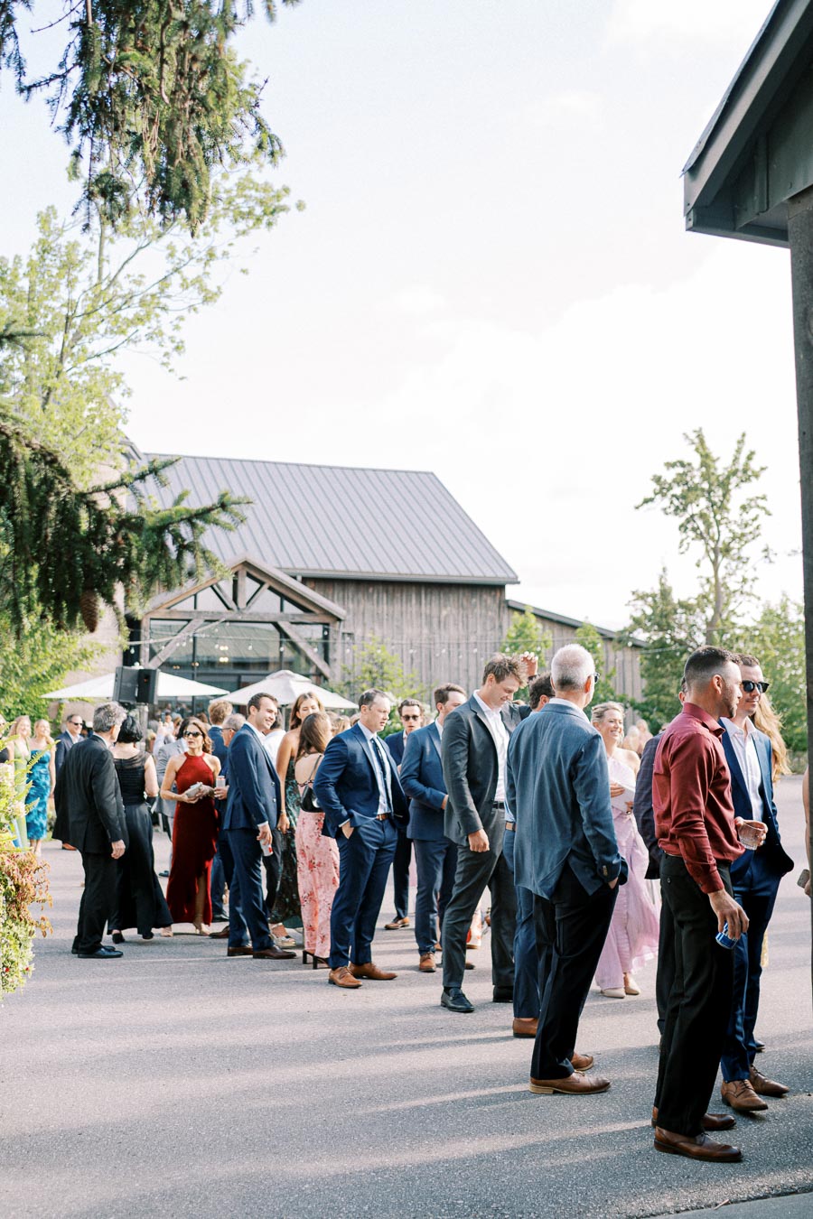 A group of well-dressed people mingling outdoors at an elegant event near a rustic barn venue.