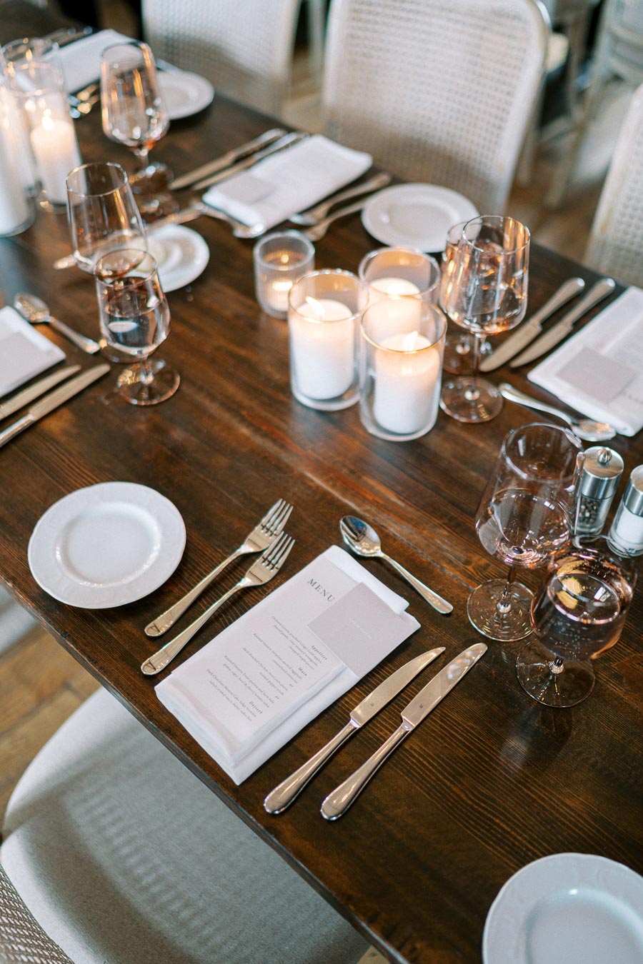 Elegant dining table setting with lit candles, crystal glassware, neatly arranged cutlery, and white plates, creating a sophisticated ambiance for a formal dinner.
