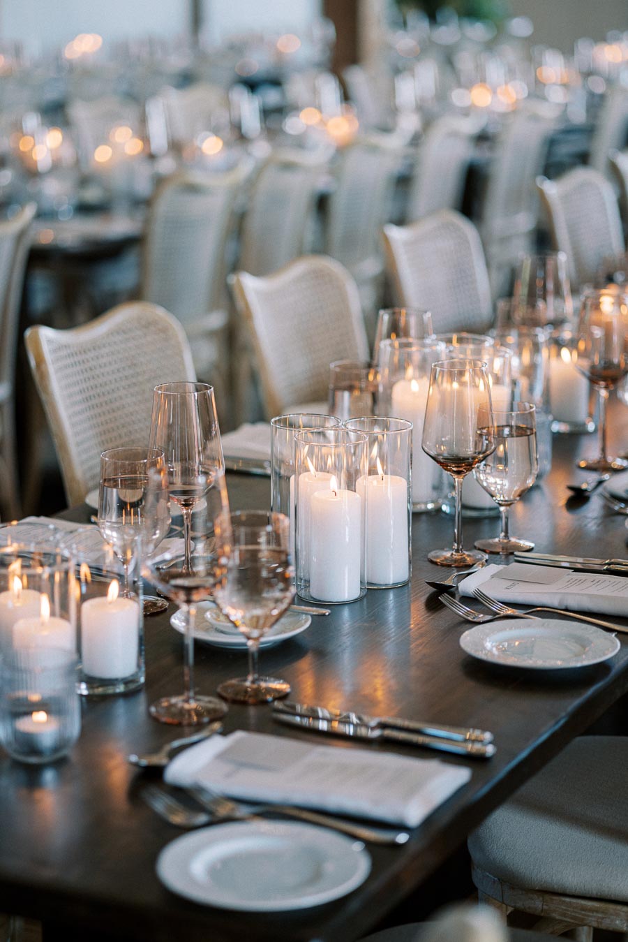 Elegant table setting with lit candles and wine glasses on a dark wooden table, creating a warm and inviting atmosphere for an upscale event or dinner party.