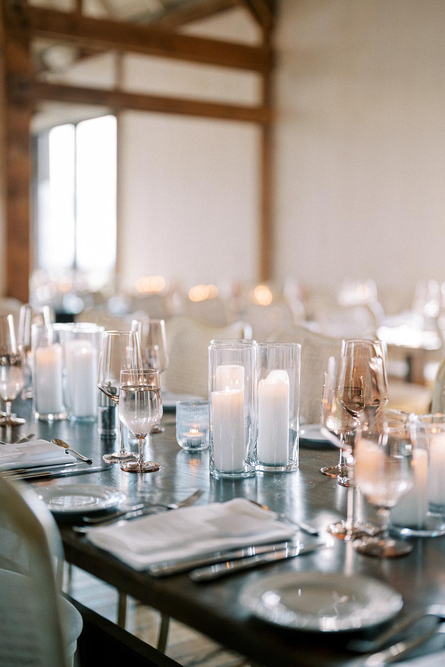 Elegant table setting with white candles in glass holders, wine glasses, and neatly arranged plates at a fine dining restaurant.