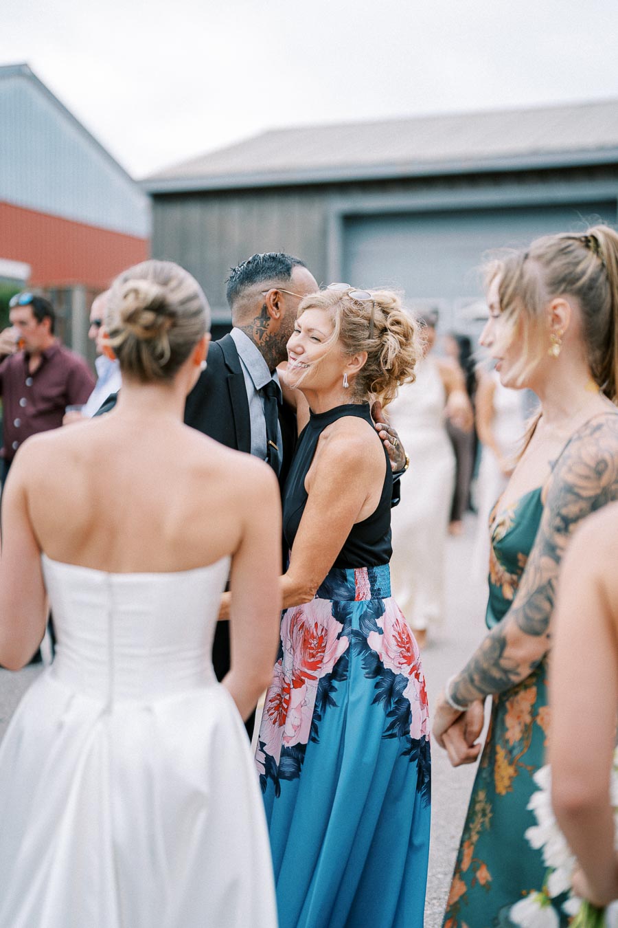 Outdoor wedding reception with elegantly dressed guests mingling; one woman in a floral skirt and a man in a suit are enjoying a conversation amidst a festive atmosphere.