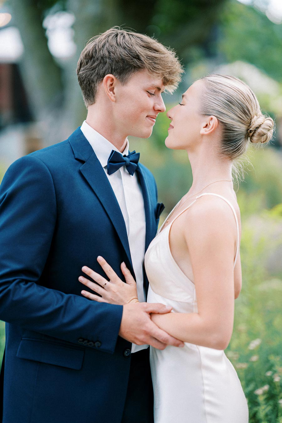 A couple in elegant attire embracing tenderly outdoors in a romantic setting, highlighting a loving moment.