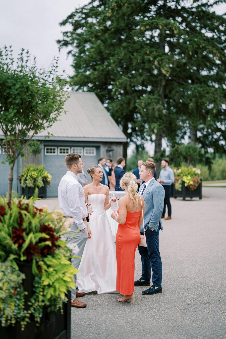 Outdoor wedding reception with guests socializing in formal attire, surrounded by lush greenery and elegant decor.