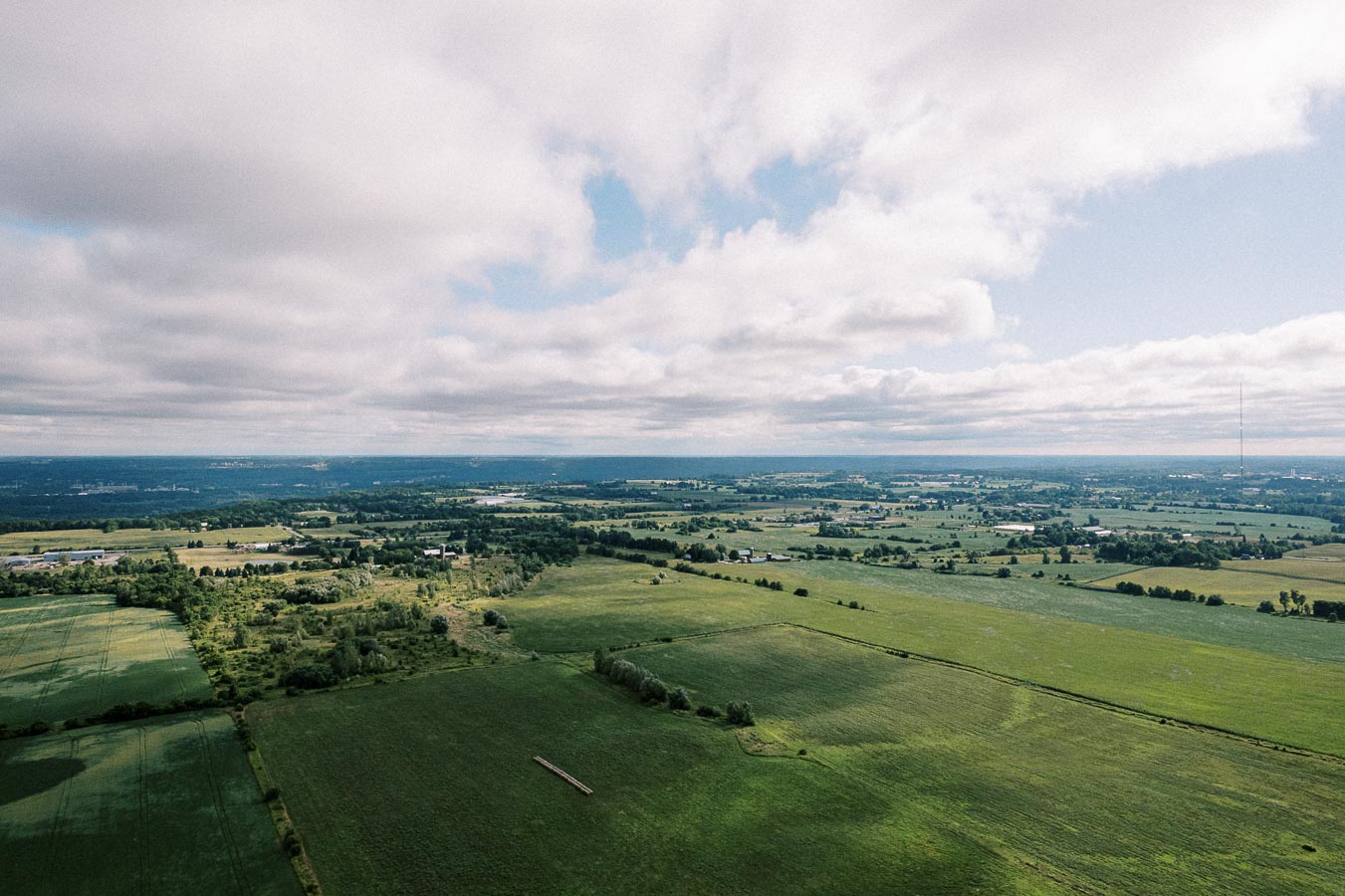 Aerial view of expansive green fields and farmland under a partly cloudy sky, showcasing the vast rural landscape and agricultural scenery.
