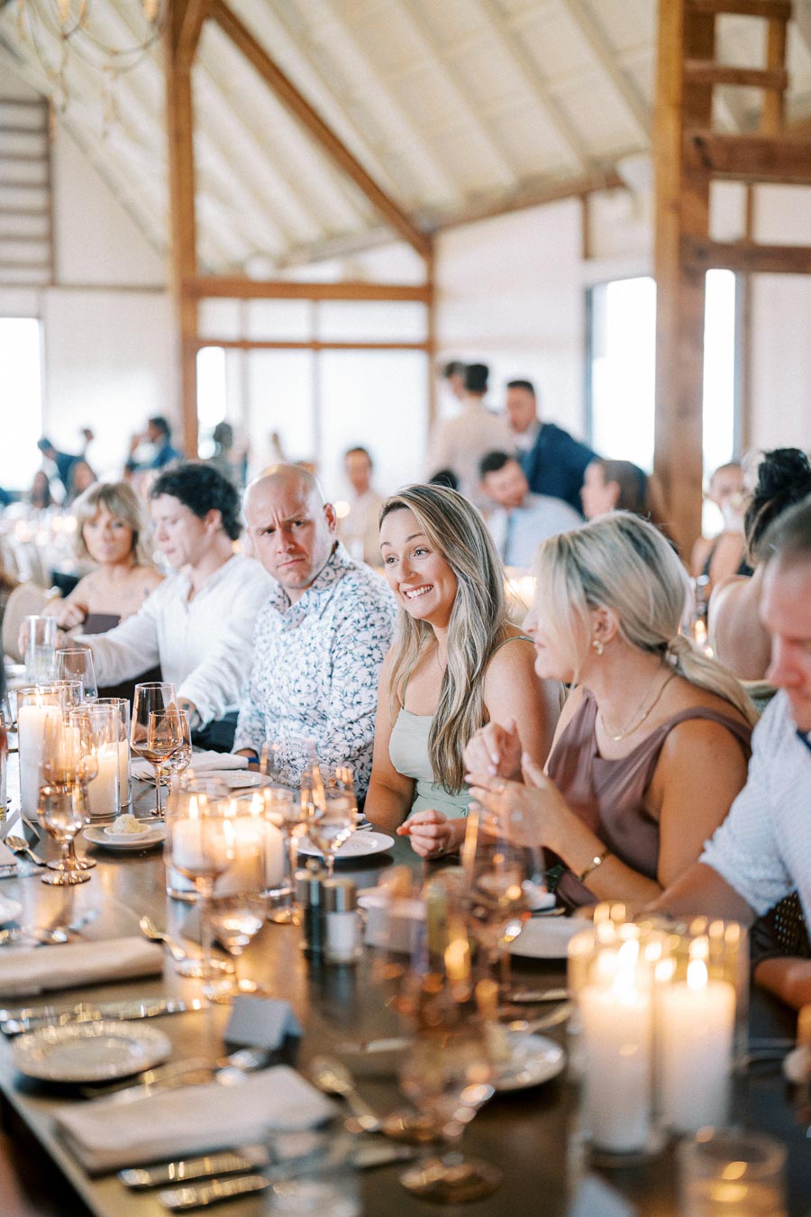 Elegant dinner gathering with people seated around a beautifully set table, featuring lit candles and glassware in a warmly lit venue for a special occasion.
