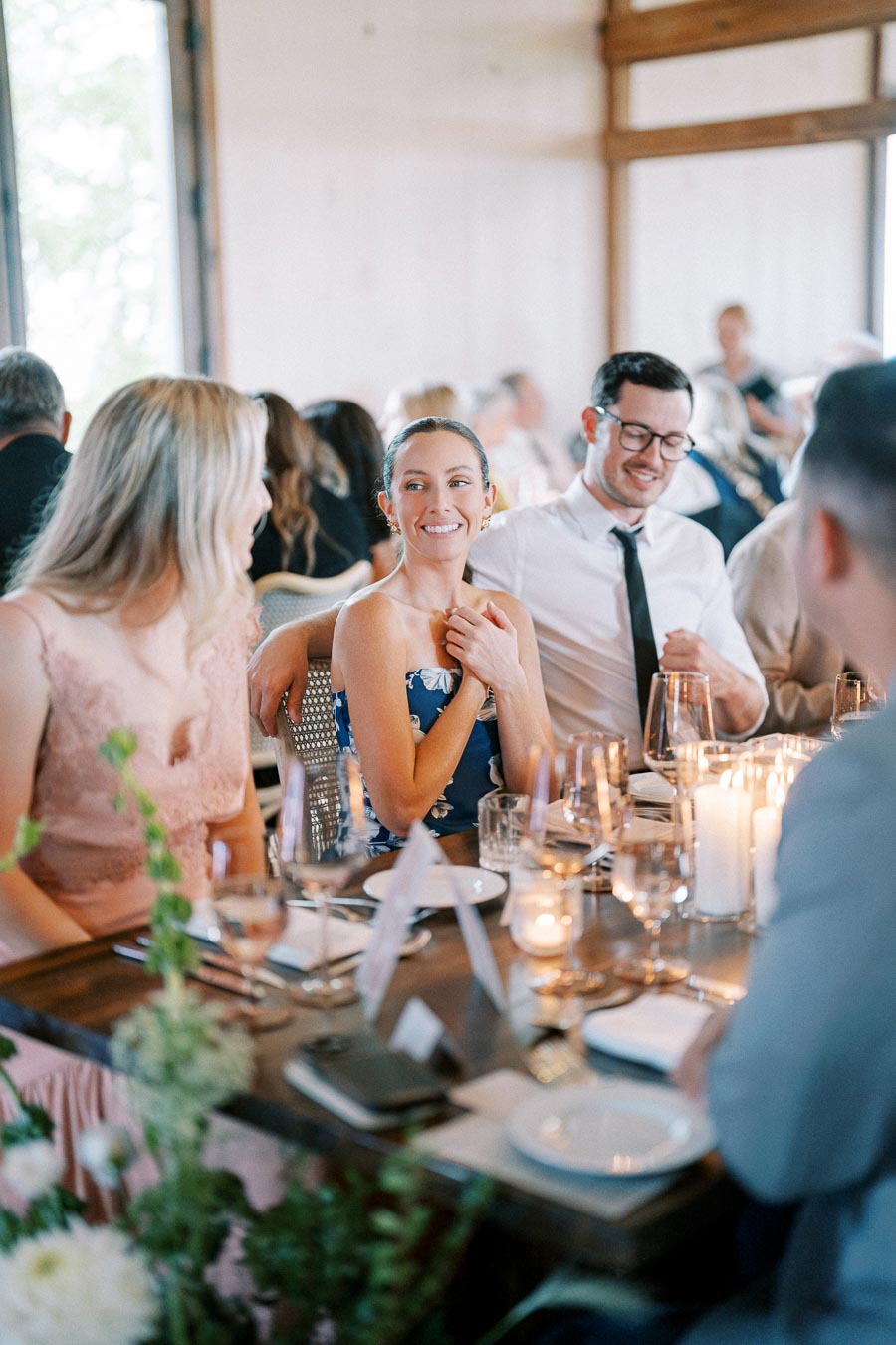Guests enjoying a joyful dinner gathering, seated at a candlelit table, engaging in conversation at an event.