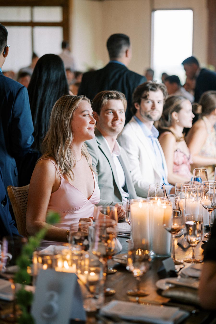A group of people in formal attire enjoying a candlelit dinner at an elegant indoor event, with beautifully arranged table settings and a lively atmosphere.