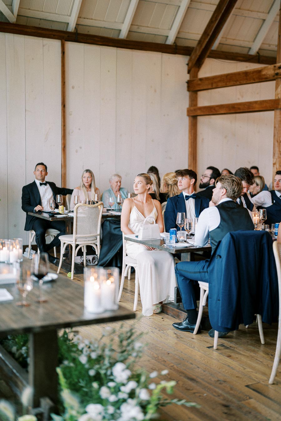 Guests seated at elegantly decorated tables during a formal event in a rustic venue, with candles and flowers adding to the ambiance.